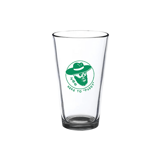 Clear glass pint glass with a green logo featuring a bearded face in a hat and the text ’HERE TO PADDY’.