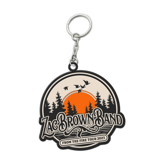Keychain featuring a circular logo for Zac Brown Band’s ’From the Fire Tour 2023’ with a forest and sunset design.