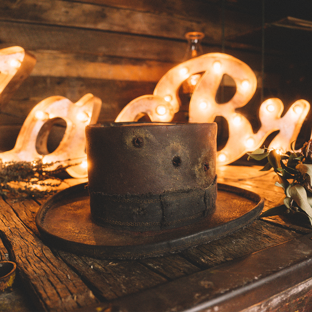 Worn, weathered top hat sitting on a wooden surface.