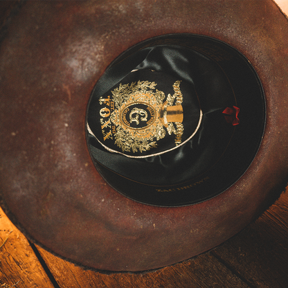 Black cowboy hat with an ornate gold emblem on the band.
