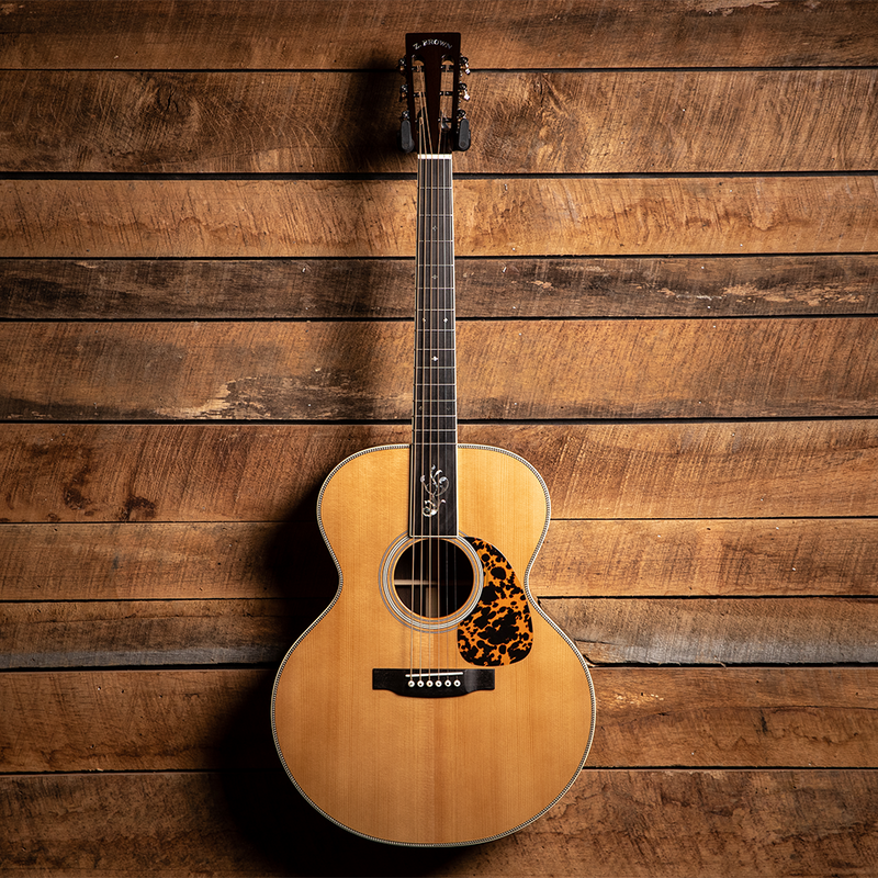 Acoustic guitar with a natural wood finish and tortoiseshell pickguard hanging on a wall.