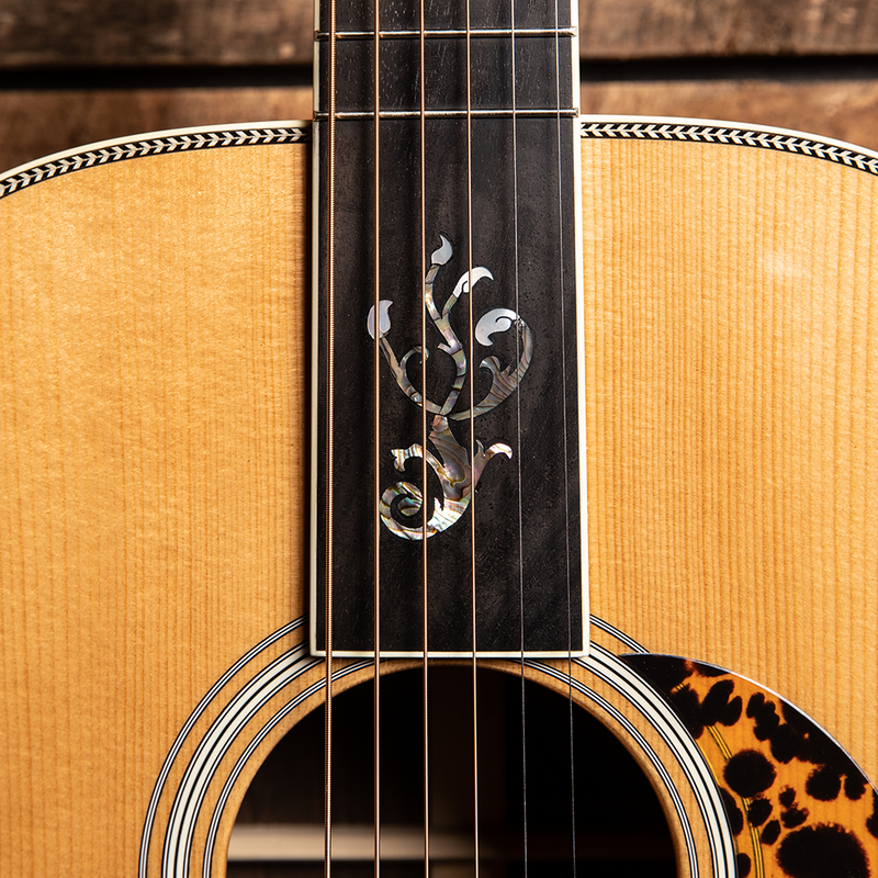 Acoustic guitar with decorative floral inlay on the fretboard and a tortoiseshell pickguard.