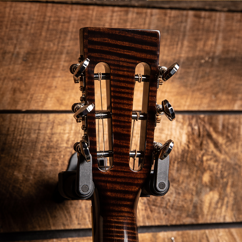 Guitar headstock with tuning pegs against a wooden background.