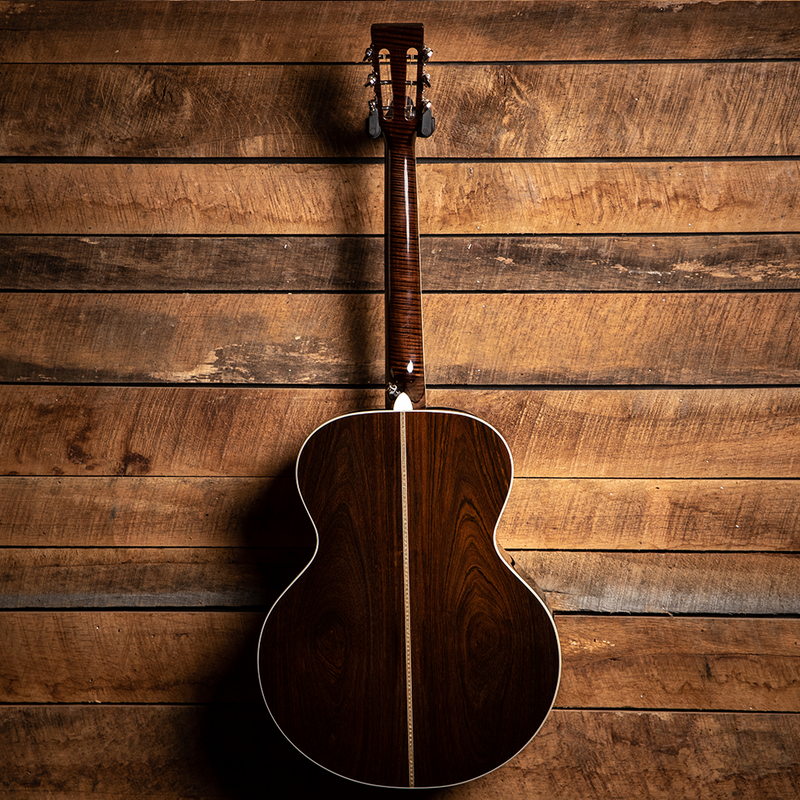 Acoustic guitar with a dark wood body hanging against wooden planks.